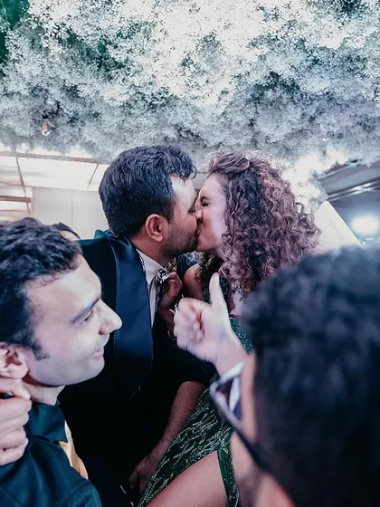 A sweet moment as a couple kisses amidst the celebration, surrounded by their cheering friends.