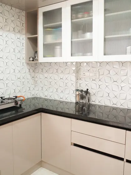 A wider view of the kitchen with the 3D geometric backsplash, paired with off-white lower cabinets and a black granite countertop. The design is minimalist yet full of interesting details.