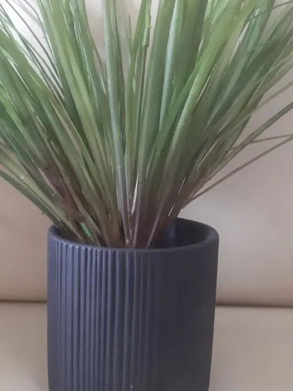 A simple yet elegant black ceramic planter with a vertical ribbed texture. It's a versatile piece that works well for holding artificial grasses or succulents in a modern setting.
