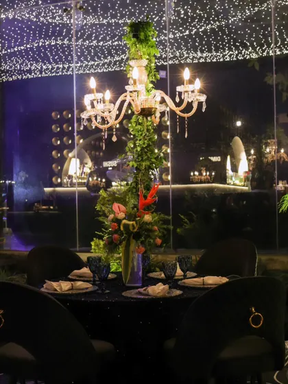 An intimate table setting with a candelabra centerpiece entwined with greenery, looking out onto the main event space through a glass wall.
