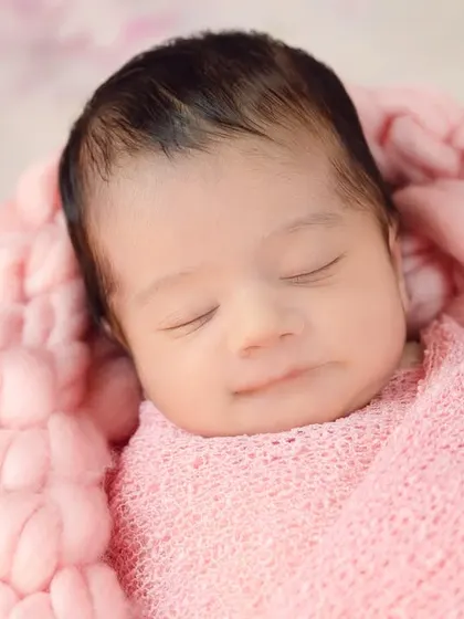 A close-up of a newborn's sweet, sleeping face, wrapped in a soft pink blanket. These are the quiet, serene moments you'll want to remember forever.