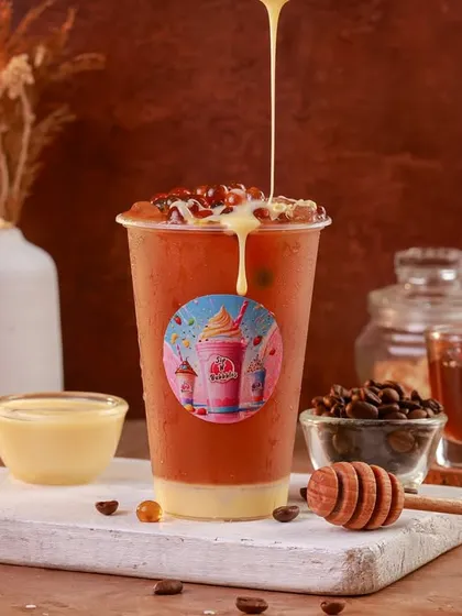 An iced coffee or bubble tea with a creamy drizzle, styled with coffee beans and a honey dipper for a rich, cafe-style shot.