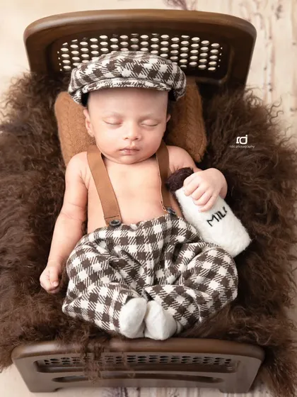 This little fellow in his checkered pants and cap, holding a milk bottle, looks like he's from a classic storybook. A truly timeless and charming newborn pose.