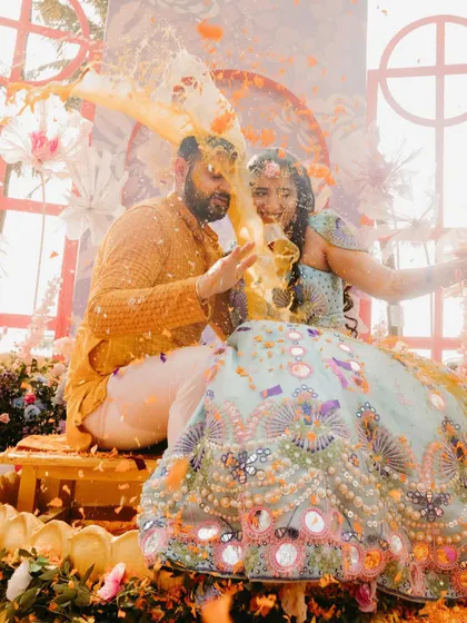 A playful moment during a Haldi ceremony, with a splash of turmeric water being thrown at the couple.