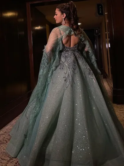 The back view of our mint shimmer organza flared gown. This shot highlights the dramatic cape veil that flows from the shoulders, adding an ethereal and glamorous touch to the sparkling, crystal-encrusted dress.
