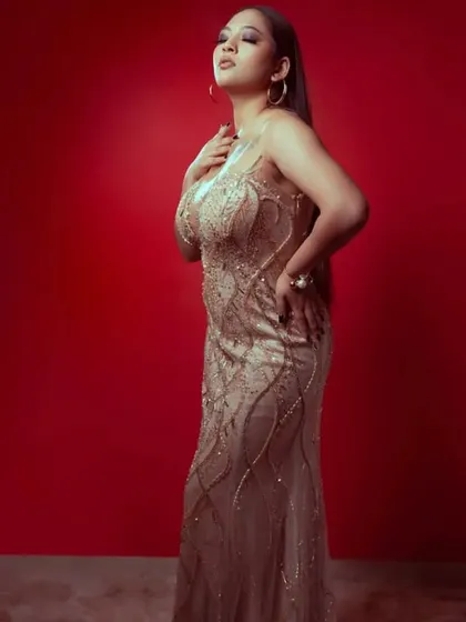 A full-length shot of the champagne gold gown against a bold red background, highlighting its intricate wave-like sequin pattern.