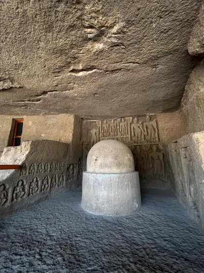 A stone stupa inside one of the smaller cave chambers, surrounded by carved reliefs on the walls.