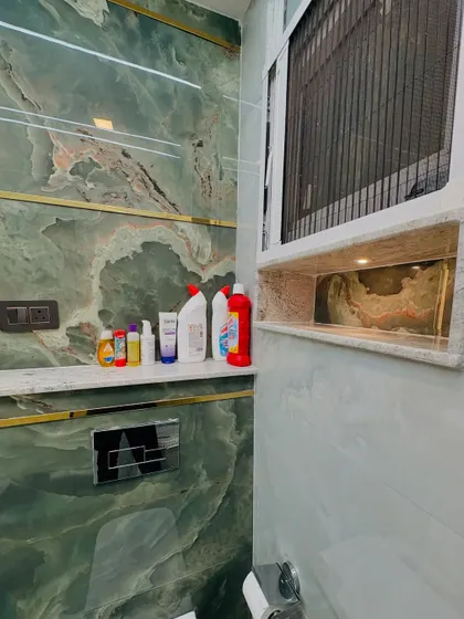 A close-up of a bathroom with green onyx-style tiles and gold inlay. This image highlights the built-in niche for toiletries and the modern, concealed flush system.
