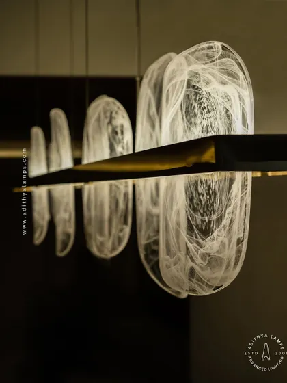 This linear pendant features organic, rounded glass elements with a beautiful white smoke effect inside. Suspended from a simple gold bar, it provides a soft, ethereal glow, ideal for creating a serene atmosphere over a dining table.