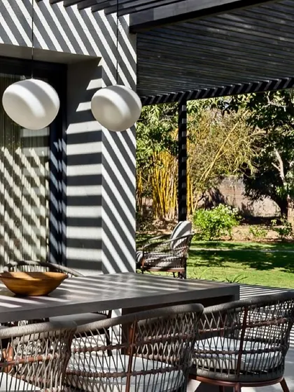 A detail of the outdoor dining setup at the Mango Orchard House, where the graphic shadows from the pergola become a key design element.