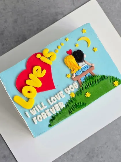 A sweet, rectangular "Love Is..." cake, perfect for anniversaries or Valentine's Day. This design uses fondant cutouts to create a charming, illustrative scene.