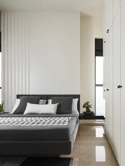 In the Slate Bedroom, a curved fluted wall detail adds subtle texture, contrasting with the clean lines of the white floor-to-ceiling wardrobes. The minimalist design is softened by plush, comfortable elements.