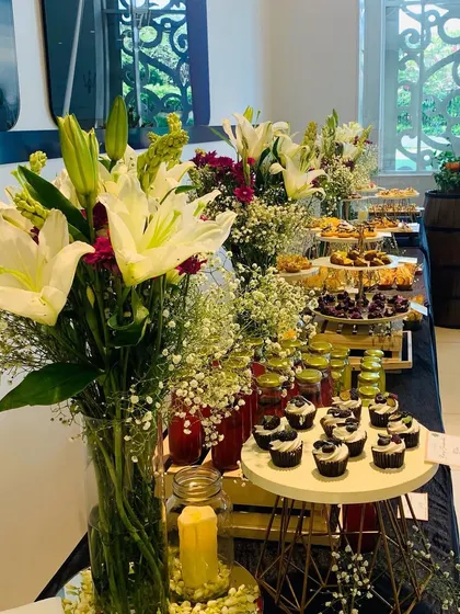 A beautiful dessert and beverage table setup at the Taj Santacruz. The display is enhanced with a large, elegant centerpiece of fresh white lilies and other seasonal flowers.
