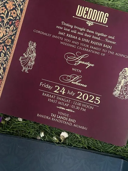 A wedding insert with a rich maroon background and elegant gold script, featuring a traditional floral border on the side.