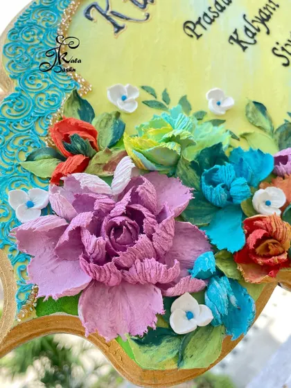 A close-up of the "Kulkarni's" nameplate, showing the intricate petals of the large lavender peony and the surrounding smaller flowers.