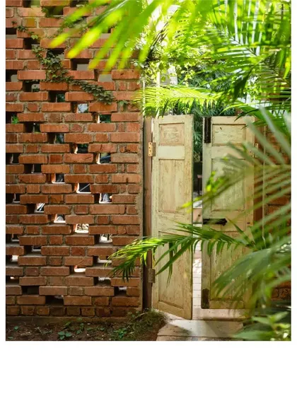 A light green vintage door opens into a garden, framed by a perforated brick wall that allows light and breezes to pass through.