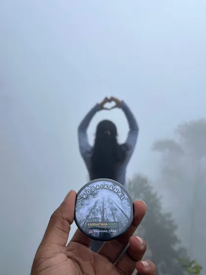 A creative shot of our Kodaikanal badge with a trekker making a heart shape in the misty background.
