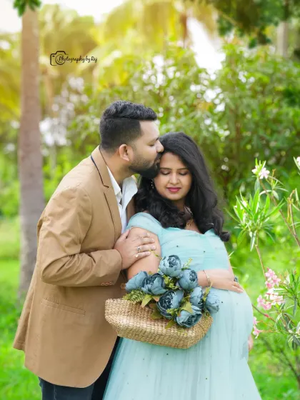 A sweet couple's portrait in a garden, with the mother-to-be in a light blue gown holding a basket of flowers.