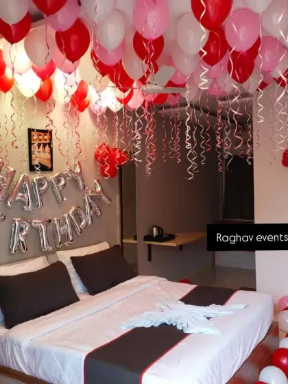 A simple and sweet birthday room decoration in a hotel. The setup includes red, pink, and white balloons on the ceiling and 'Happy Birthday' foil letters.