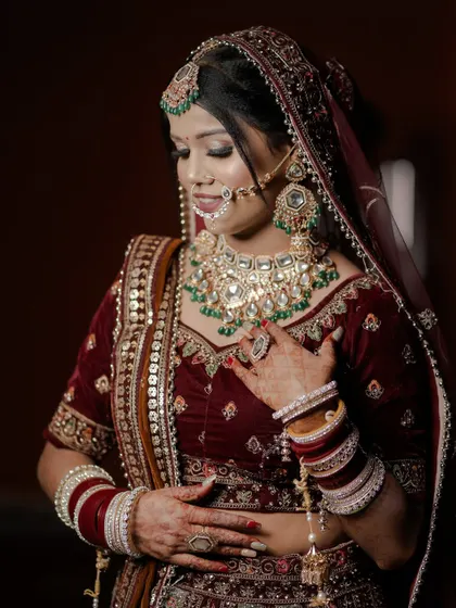 A close-up portrait of a bride, showcasing her elegant posture and the stunning green and white Kundan jewelry set against her velvet lehenga.