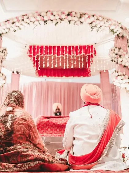 A serene moment from a Sikh wedding, showing the couple during the Anand Karaj ceremony from a respectful distance, with the beautiful mandap in the background.