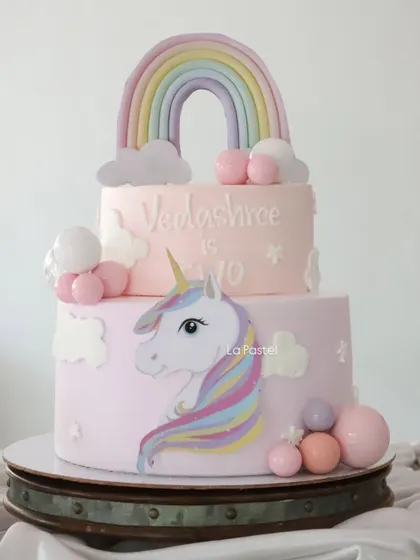 A magical two-tier unicorn cake for a second birthday. I used soft pastel colors for the rainbow and unicorn, adding fluffy clouds and colorful spheres to complete this dreamy design.