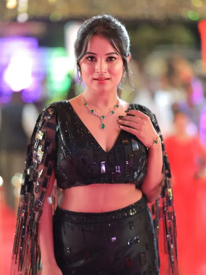 Anusha Rai posing with her hand on her neck, drawing attention to her elegant jewelry.