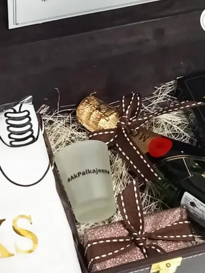 A luxurious groomsman hamper in a brown leather-style box, featuring a bottle of Moët, a personalized shot glass, and a custom t-shirt.