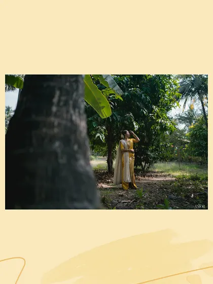 An artistic shot of the bride in a natural setting, framed by a tree trunk. This composition creates a sense of scale and highlights the beauty of the outdoor venue.