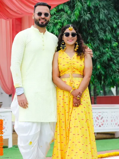 A happy couple portrait from their Haldi day. Their coordinated yellow and white outfits and sunglasses give off a cool, celebratory vibe.