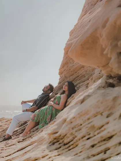 A relaxed moment with the couple resting against a unique rock formation by the sea, gazing up at the sky.