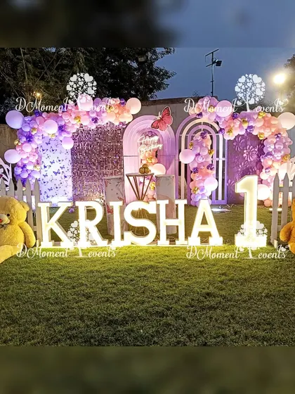 An outdoor butterfly-themed first birthday setup, featuring a beautiful stage with marquee letters, oversized teddy bears, and a white picket fence for a charming garden party feel.