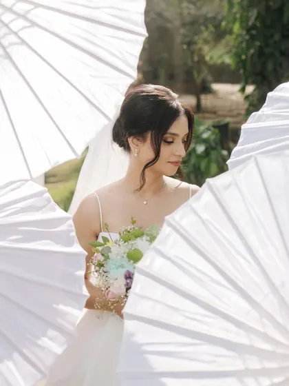 An artistic portrait of the bride framed by white parasols, creating a soft and dreamy look.