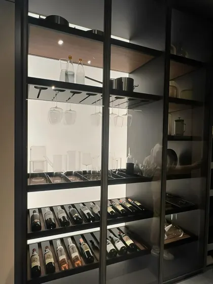 A custom-designed wine cellar and bar storage unit. The sleek, black-framed glass doors, integrated lighting, and dedicated racks for bottles and glassware combine sophisticated aesthetics with practical functionality.