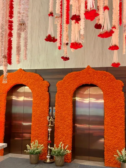 A view showing the marigold-covered elevator arches with hanging floral tassels above. This combination of ceiling and entrance decor creates a fully immersive, traditional atmosphere for a Mehendi or Haldi ceremony.