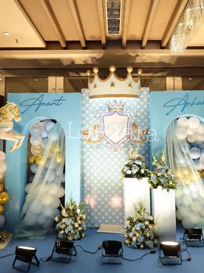 A carousel-themed stage with a regal blue and gold color scheme. The backdrop features leaping carousel horses and a central crest, creating a dynamic and whimsical setting for a prince's birthday.