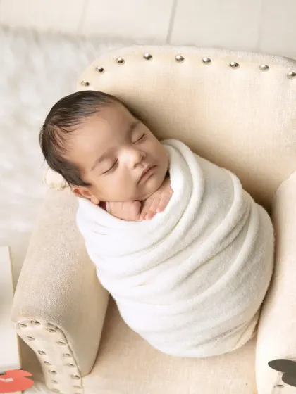 This pose, often called the "potato sack" wrap, keeps the baby snug and secure, allowing for these adorable, sleepy portraits in our miniature chair.