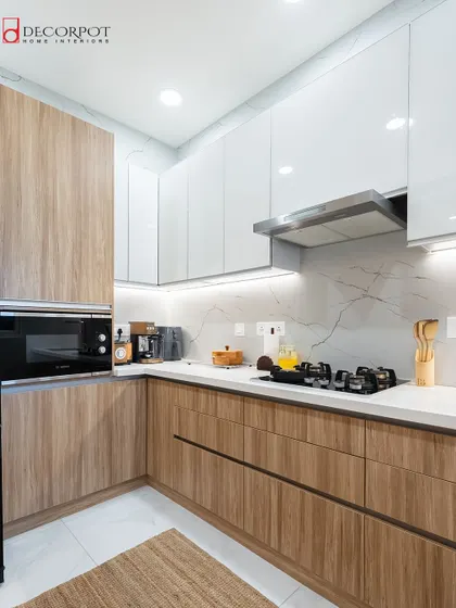This L-shaped kitchen showcases a beautiful contrast between natural wood-textured laminate and clean white high-gloss cabinets. The design provides an efficient workspace while maintaining a warm and inviting atmosphere.