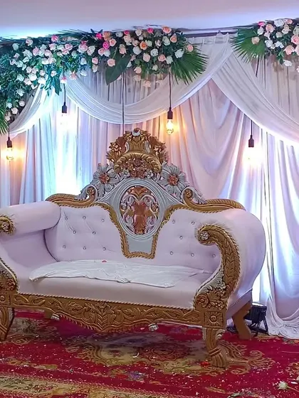 A simple and elegant stage setup with white drapery and hanging floral arrangements. The classic sofa and minimalist design are perfect for intimate engagements or receptions.