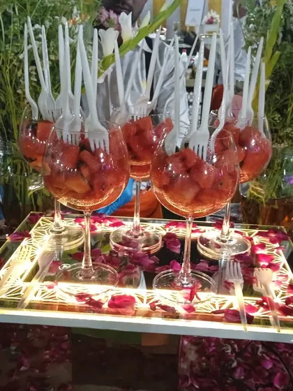 A tray of watermelon salad glasses, garnished with fresh flowers and rose petals, ready for service.