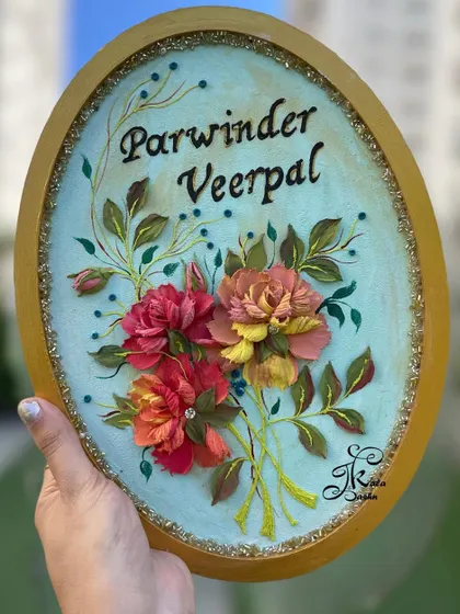 A beautiful anniversary gift. This oval nameboard features a bouquet of sculpted peonies in shades of red and peach, with delicate buds and leaves creating a sense of natural movement around the couple's names.