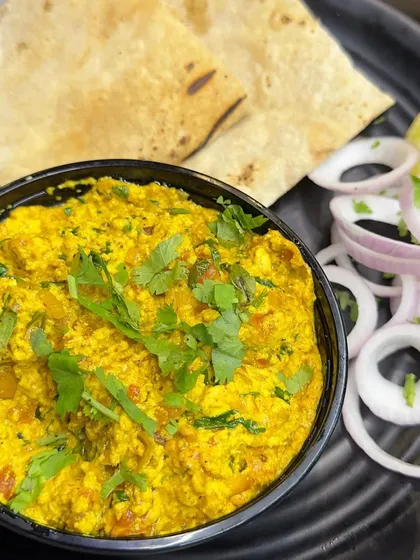 A classic plate of Paneer Bhurji, garnished with fresh coriander and served with sliced onions and a lemon wedge.