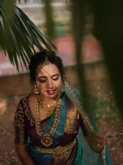 A candid moment captured beautifully. The soft, diffused lighting highlights the glowing skin and the intricate details of her temple jewellery and traditional South Indian bridal attire.