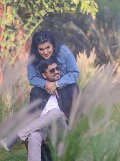 A playful and romantic outdoor pre-wedding photo, capturing the couple's interaction among tall, feathery grass.