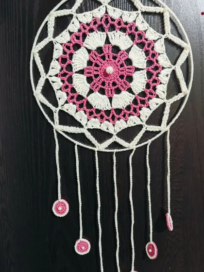 A full view of the pink and white dreamcatcher, showing the delicate hanging threads with small crocheted circles. A perfect piece for a serene bedroom.