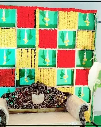 A colorful checkerboard backdrop made with panels of red, yellow, and green, decorated with marigold flowers. This is a popular and vibrant choice for Haldi, Mehendi, or baby shower events.
