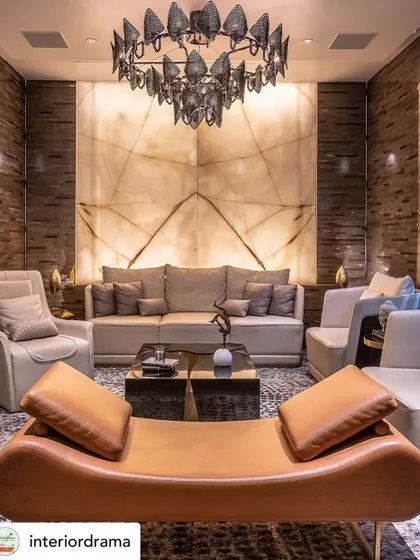 This living room, featured by Interior Drama, showcases an onyx backdrop that adds a significant luxe quotient. The backlit natural stone becomes the focal point, complemented by a sculptural chandelier and a mix of leather and fabric seating.