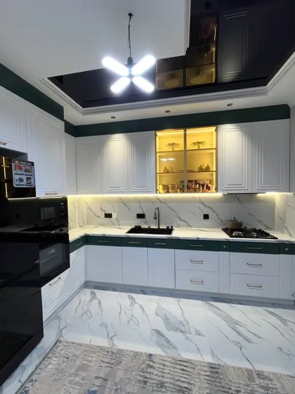 A wide-angle view of the luxurious green and white classic kitchen, showing the overall L-shaped layout, the marble-look flooring, and the stylish ceiling and lighting design.