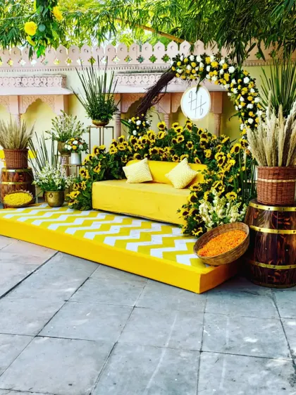 A chic poolside Haldi setup featuring a yellow sofa on a chevron-patterned stage, surrounded by sunflowers and rustic barrels.