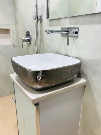 A close-up of the stylish vessel sink, which has a metallic, patterned exterior. It sits atop a simple white vanity, and the faucet is wall-mounted for a clean, modern look.